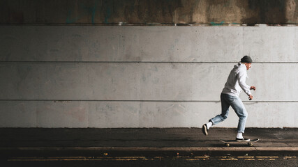 Man skateboarding under a bridge with urban wall design space - Powered by Adobe