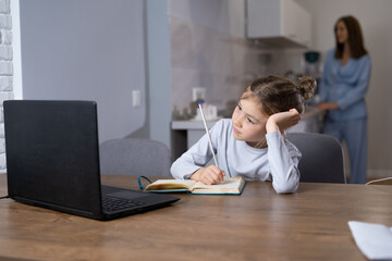 young beautiful schoolgirl is sitting at the table at home. tired look of a schoolgirl during remote learning