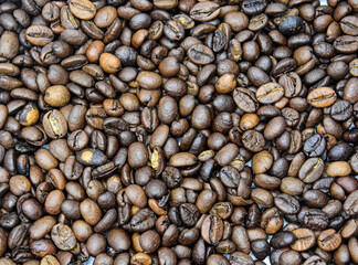 Top view abstract background of lots of small dark brown coffee beans in daylight 


