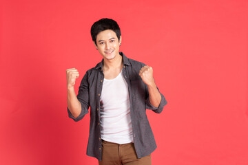 Happy young asian man in casual dress celebrates with two hand in the air on isolate red background.
