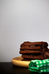 Chocolate cookies are placed in a wooden tray with a green cloth placed over a black background.
