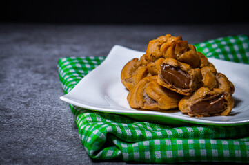 Put the chocolate filling cream in a white plate on top of a green patterned cloth set on a cement table.