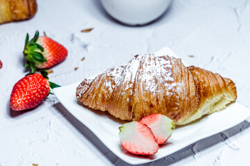 A continental breakfast consisting of croissants sprinkled with icing sugar and fresh strawberries.