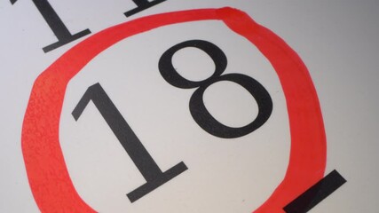 18 - Marking the date in the calendar with a red marker. The eighteenth day of the month. The hand circles the date in the calendar with a pen. Number in the red circle close up