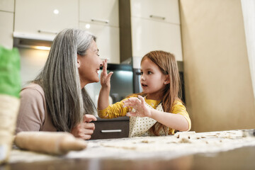 Little granddaughter smearing flour on laughing grandmother nose