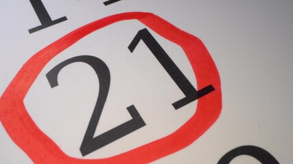 21 - Marking the date in the calendar with a red marker. The  twenty first day of the month. The hand circles the date in the calendar with a pen. Number in the red circle close up