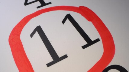 The hand circles the date in the calendar with a pen. Number in the red circle close up. 11 - The eleventh day of the month