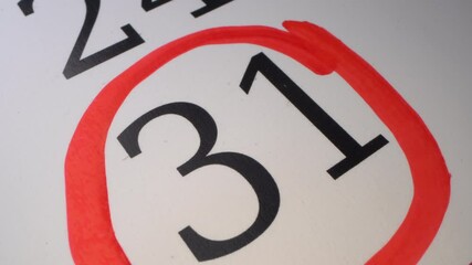31 - The hand circles the date in the calendar with a pen. Number in the red circle close up. The thirty-first day of the month