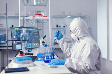 Engineer in microbiology lab holding micropipette with sample from test tube. Chemist in modern laboratory doing research using dispenser during global epidemic with covid-19.