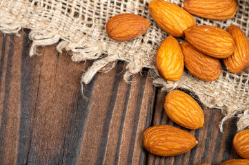 Almonds are scattered on a wooden table covered with a homespun cloth with a rough texture.