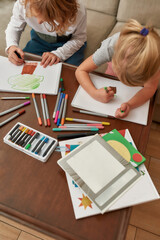 High angle view of focused little kids, boy and girl drawing on paper using marker pen, sitting together on a couch at home