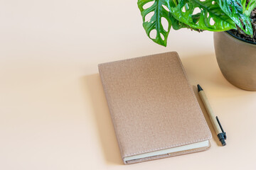 Mockup photo with time diary and a pen on the beige background. Display planner at an angle, showing material and color. Blank for displaying your text or logo.