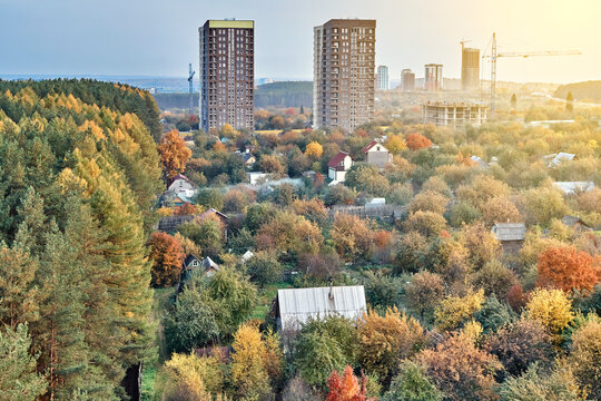 Contemporary highrise city dwelling buildings annex territory of neat summer cottages among colorful autumn trees at sunset