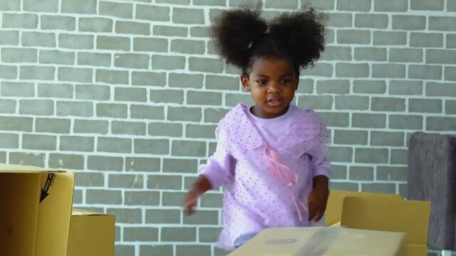 Happy cute active little African American girl fun to playing by fighting to carton box in living room and she look happiness for playing in her home