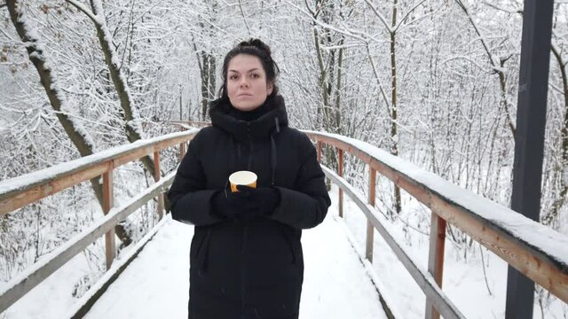 Beautiful young girl walks in winter in the park with a glass of coffee in her hands