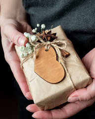 Gift box wrapped in craft paper decorated with wooden heart and white flowers in human hands. Valentine day celebrating. space for text