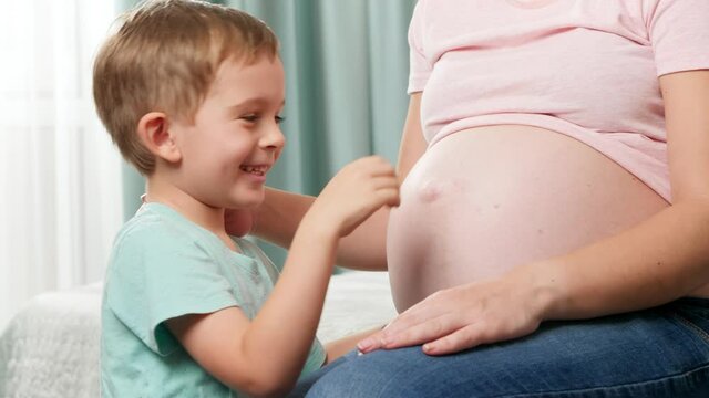 Smiling happy little boy tickling and having fun with big pregnant belly of his mother