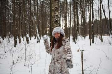 young woman plays snowballs in winter nature. Girl is dressed in a beige down-padded coat and knitted gray hat.