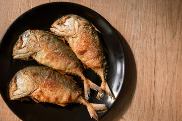 Top view dish of three fried mackerels on wooden table.