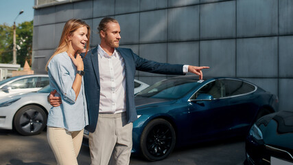 Fototapeta na wymiar Young man and girl pointing at car in showroom