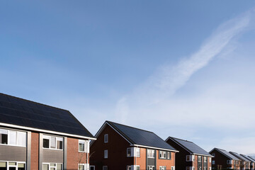 Solar panels mounted on the roofs of a row modern new-build houses in Lemmer, Friesland, the Netherlands with blue sky