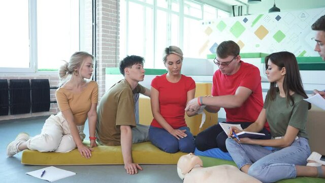 Young male instructor show how bandage a hand in a right way, group of people learn the first aid techniques.