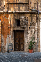 Jewish quarter, in the ghetto, detail of a wooden door of an orange building, with inserts of ancient Roman inscriptions, bas-relief of a lion, a chair and a plant, Lungotevere, Rome.