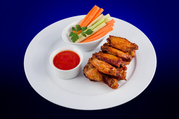 Roasted chicken wings with sticks carrots and celery and dipping sauce on white plate on blue background