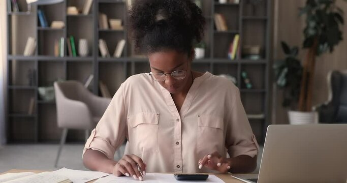 African woman in glasses sit at workplace desk calculating domestic utility bills, planning budget using computer app, making online payments, summarizing monthly expenses. Accountancy work concept