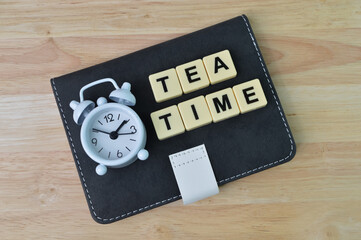 Selective focus of clock, notebook and alphabet letters with text TEA TIME.