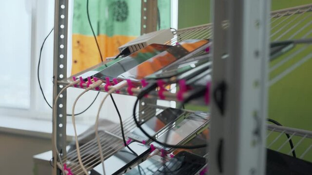 Lots of smartphones connected by wires lie on the shelf. Test bench for mobile phones or applications