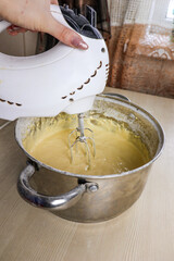 Beating the dough for baking. Woman prepares sweets at home. In hand - a mixer that mixes all the ingredients.