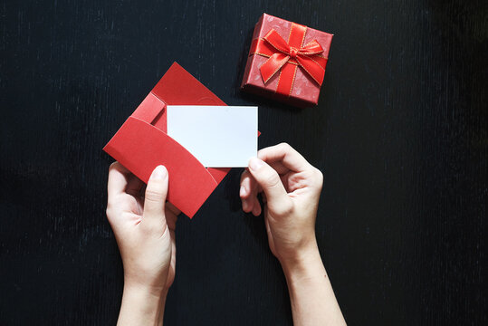 A girl puts in an envelope her Love message. Closeup image of woman puts it in an envelope letter with copy space. A gift box and a red vintage evelope on a black wooden background. Copy space.