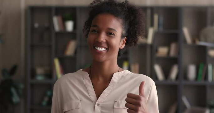 Head shot happy african businesswoman employee member standing in modern office smile look at camera showing thumb finger up. Satisfied client recommend good quality company corporate services concept