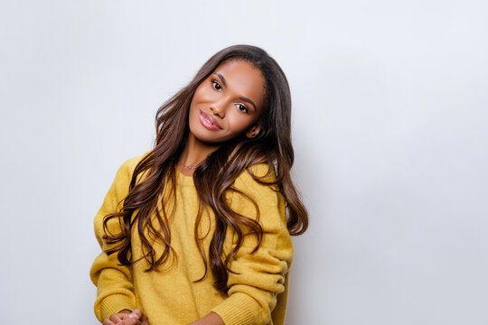 Black Girl Smile in yellow Wool Sweater looking at the camera. Portrait of beautiful black woman posing against a light wall. Beautiful latino girl student.    