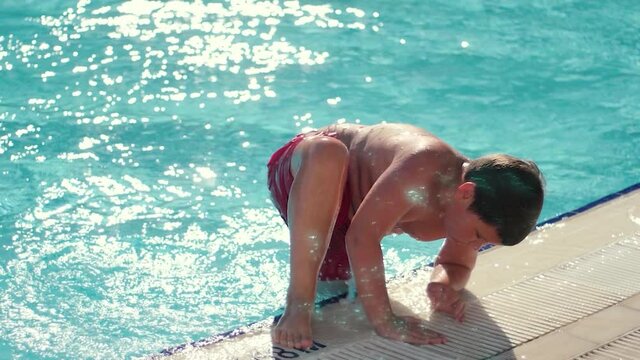 Fullness kid going out of the pool with crystal clear water in basin at sunny day. Boy relaxing during summer vacation, slow motion