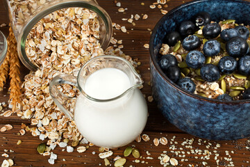 Oatmeal porridge with blueberries in a blue ceramic bowl, oat flakes and jug of vegetable almond milk on a wooden background. Healthy eating concept.