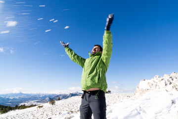 Happy brunette handsome man playing in snow wearing green hiking jacket smiling on snowy mountain