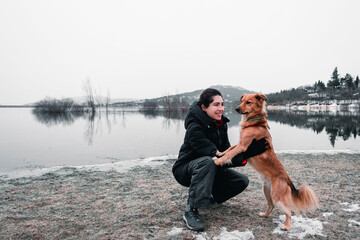 Young woman playing with her dog by the side of a lake while it snows during winter. Winter concept. Dog friend