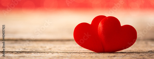 Two red hearts on wooden table and red background