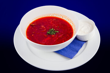 White bowl of traditional Ukrainian and Russian soup borsch or vegetable beetroot soup with sour cream on blue background