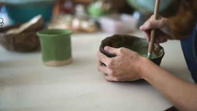 Woman mixing paint with brush inside ceramic bowl in workshop studio - Artisan work and creative craft concept - Focus on bowl