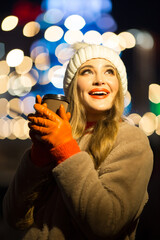 beautiful girl on the background of lights with coffee, on the street, holiday, new year. a walk through the evening city