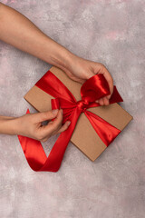 Women's hands hold a gift tied with a red ribbon on a gray background