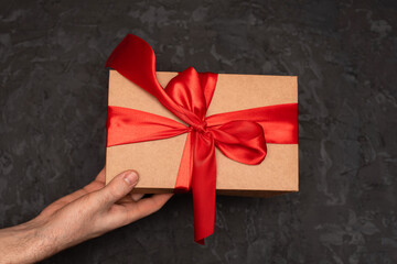 A gift box with a red bow is held in the hands of a man on a dark background