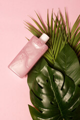 Top view of mockup of cosmetic battle with nacre textured liquid in pink color with tropical leaves