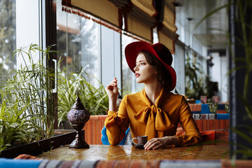 girl in a cafe with a cup of coffee and a hat. beautiful girl with a cup of coffee at the window in a cafe, waiting for a meeting, breakfast