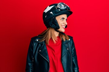 Hispanic young woman wearing motorcycle helmet looking away to side with smile on face, natural expression. laughing confident.