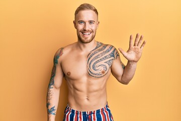 Young caucasian man wearing swimwear shirtless showing and pointing up with fingers number five while smiling confident and happy.