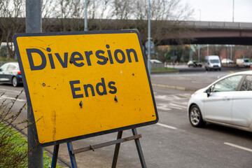 A road sign that reads diversion ends at a roundabout with cars moving in the background